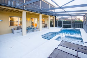 A covered outdoor swimming pool area with lounge chairs and a patio table.