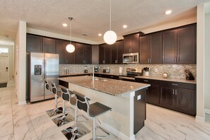 A modern kitchen with dark cabinets, stainless steel appliances, and a granite island with bar stools. - Champions Gate 1561 (Davenport)