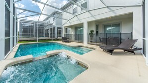 Un área de piscina interior moderna con paredes de vidrio transparente, una bañera de hidromasaje y sillones de descanso.