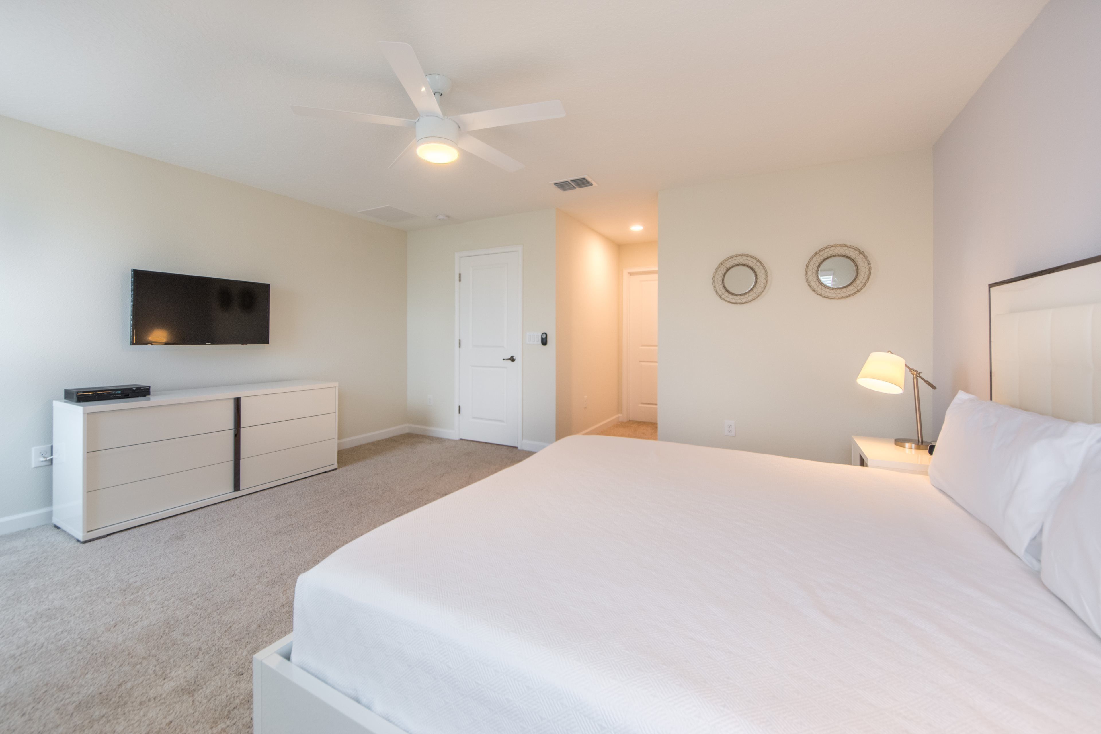 Ein Schlafzimmer mit Bett, Deckenventilator, Fernseher, Kommode und einer Tür.