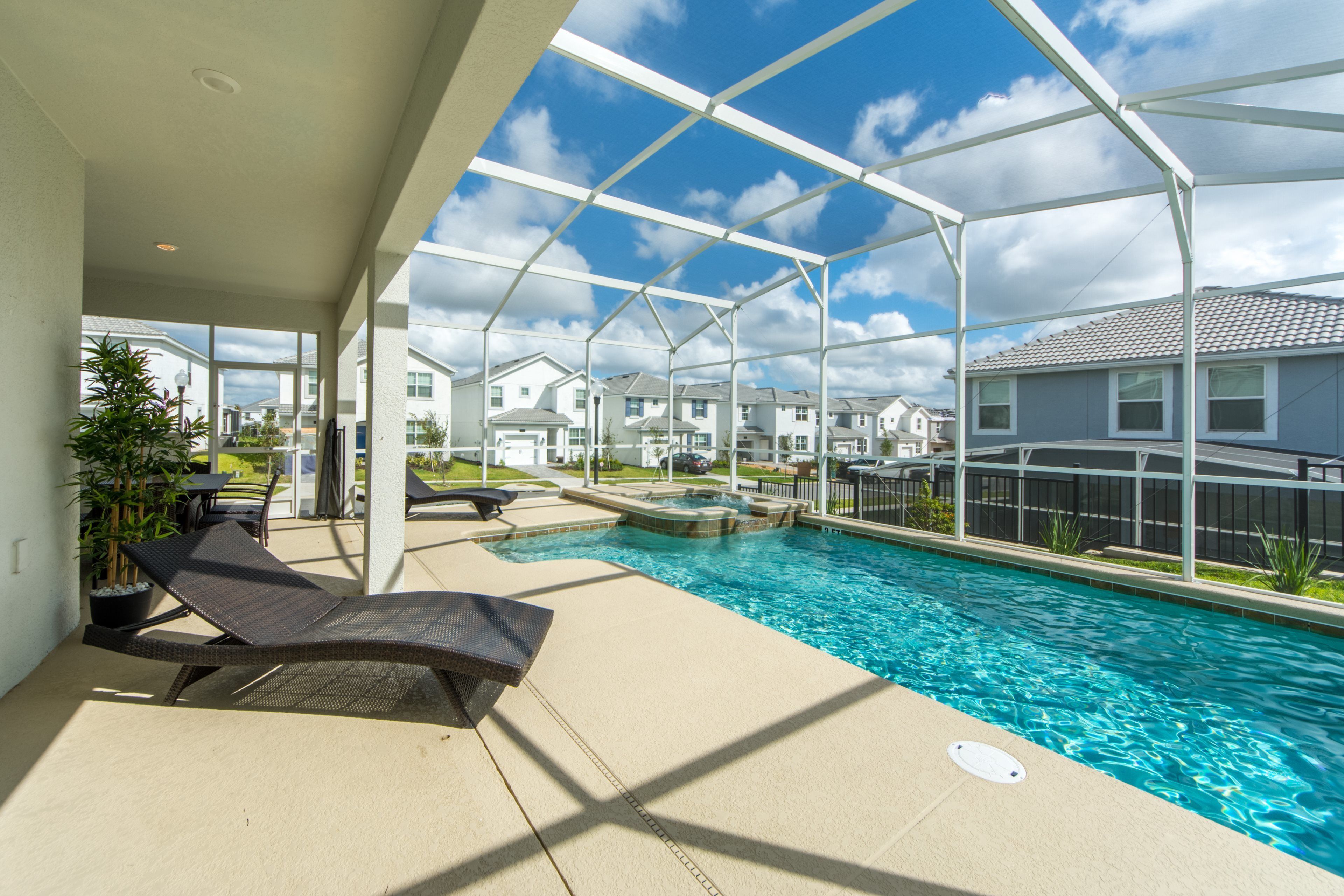 A pool area with lounge chairs, a hot tub, and a view of residential buildings.