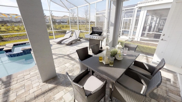 A covered outdoor area with a pool, a grill, and wicker furniture. - Champions Gate 1548 (Davenport)