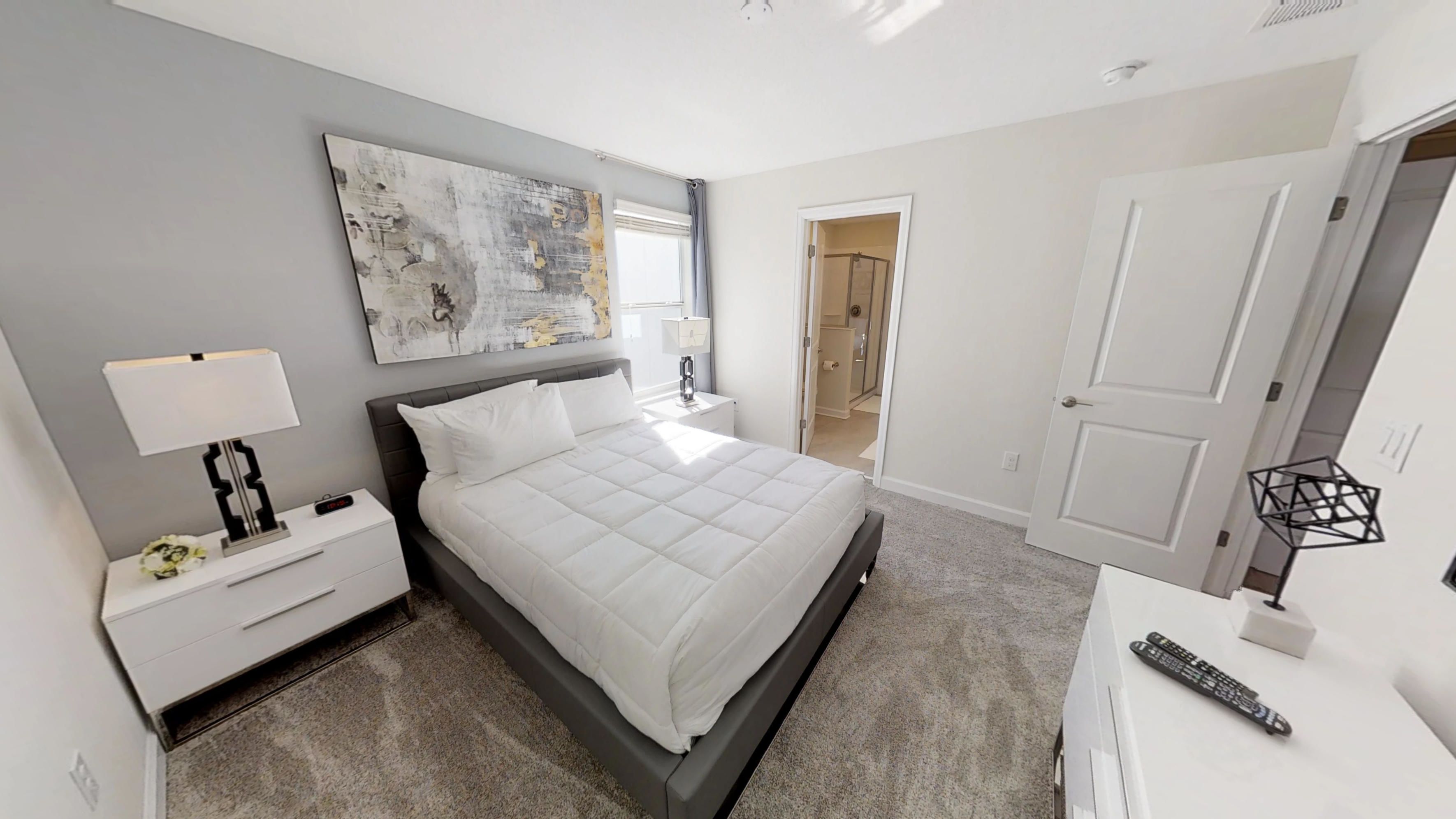 Una camera da letto con un letto, un comodino, una lampada e un quadro appeso al muro.