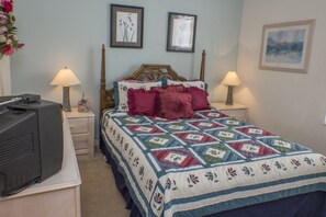 A bedroom with a bed, two bedside lamps, a dresser, and a television on a stand.