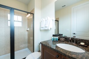 A modern bathroom with a glass-enclosed shower, a white sink, and a vanity with toiletries. - Encore Resort at Reunion 261 (Kissimmee)