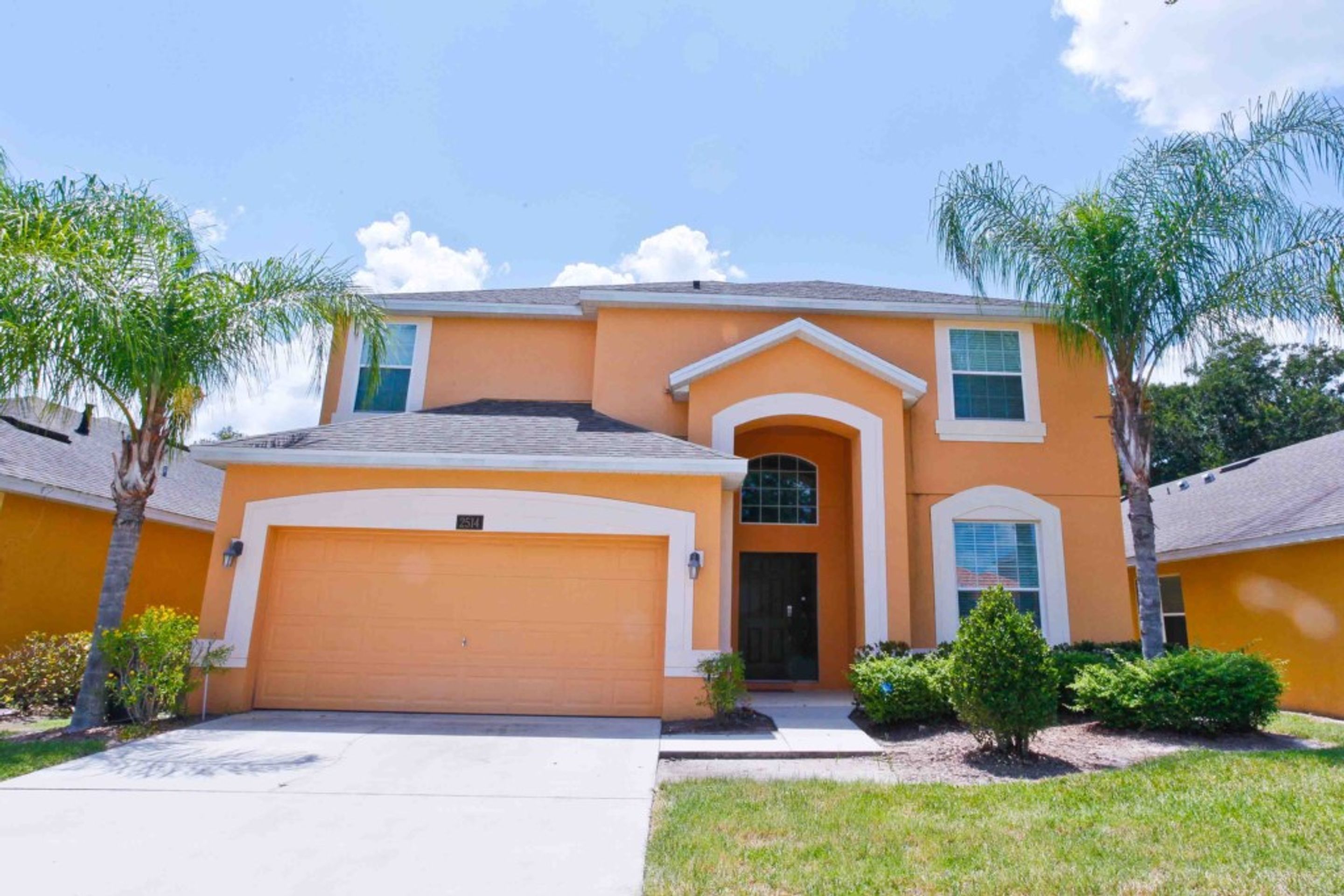 A two-story house with a garage, a front entrance with a small porch, and a well-maintained lawn with a few trees and shrubs.