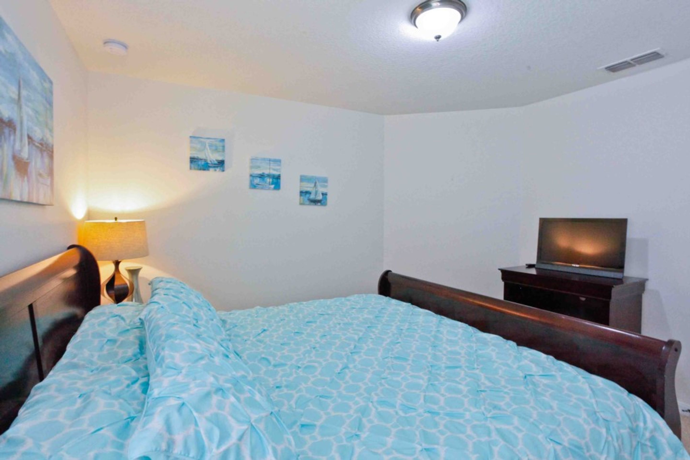 A bedroom with a bed, a TV on a stand, and a lamp on a bedside table.
