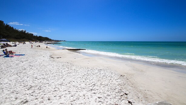 A beach with white sand, clear blue water, and a few people. - Anna Maria Island 1303 - 2 (Bradenton Beach)