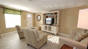 A living room with striped armchairs, a beige sofa, a TV on a white cabinet, and a window with a green valance. - Anna Maria Island 1303 - 2 (Bradenton Beach)