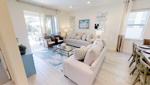A spacious living room with a white sofa, a glass coffee table, and a dining area with a wooden table and chairs. - Encore Resort at Reunion 341 (Kissimmee)