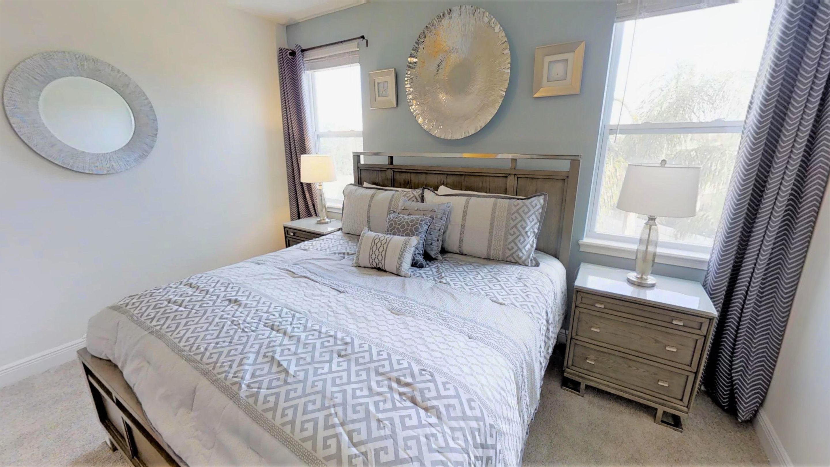 A bedroom with a bed, nightstands, a mirror, and a large decorative plate on the wall.