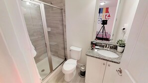 Casa de banho moderna com chuveiro em cabine de vidro, sanita branca e lavatório com bancada de granito.