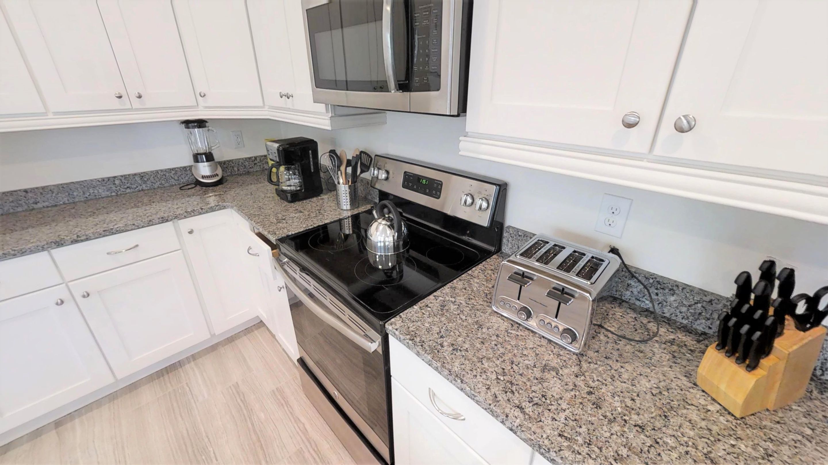 A kitchen with white cabinets, a stainless steel microwave, a kettle, a toaster, and a coffee maker.