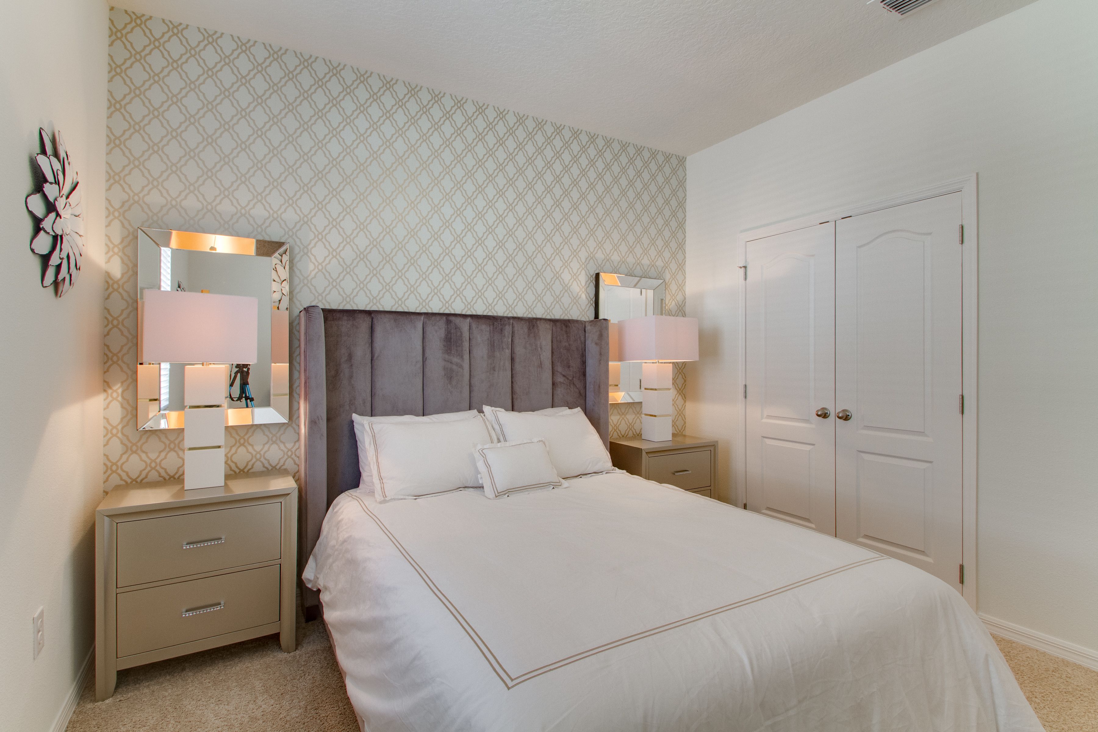 A bedroom with a large bed, two bedside tables with lamps, a wardrobe, and a patterned wall.