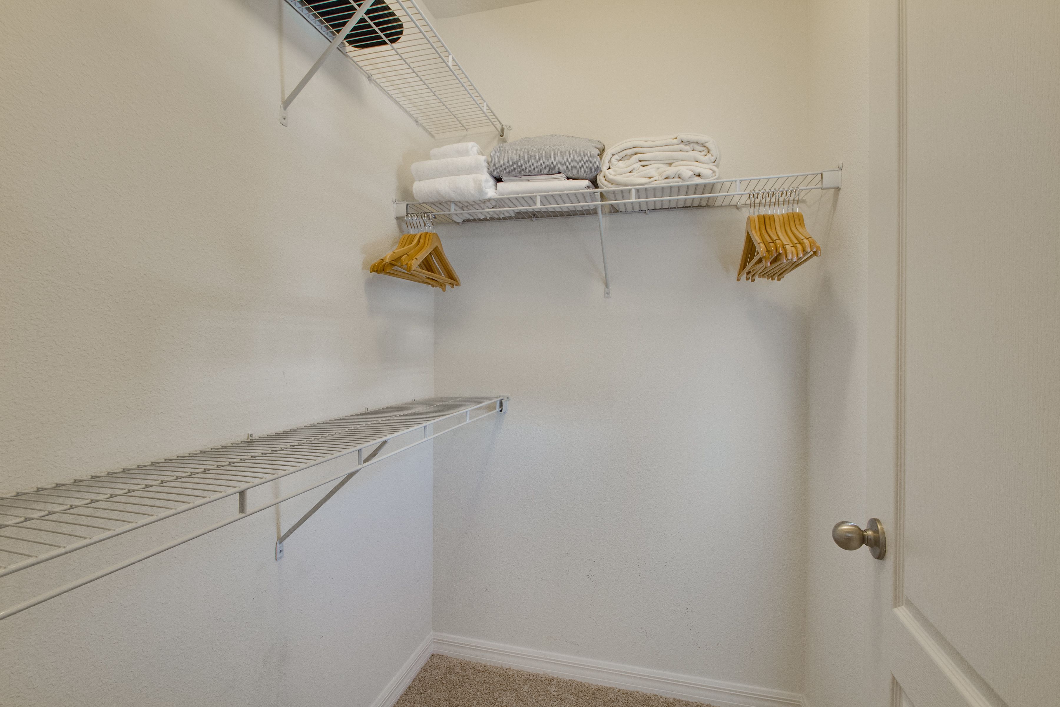 Une petite pièce aux murs blancs, avec une porte, une étagère en métal où sont pliées des serviettes et un oreiller, et une serviette jaune suspendue.