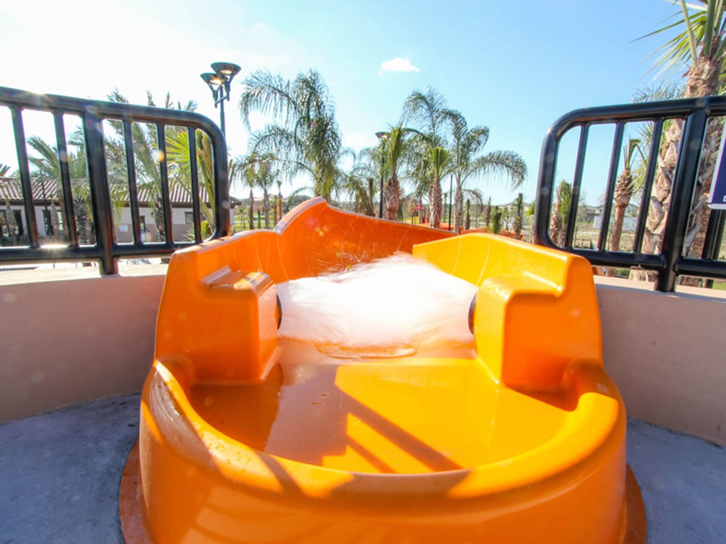 Un toboggan aquatique avec une structure jaune et un courant d’eau blanche, entouré d’une clôture métallique et de palmiers.