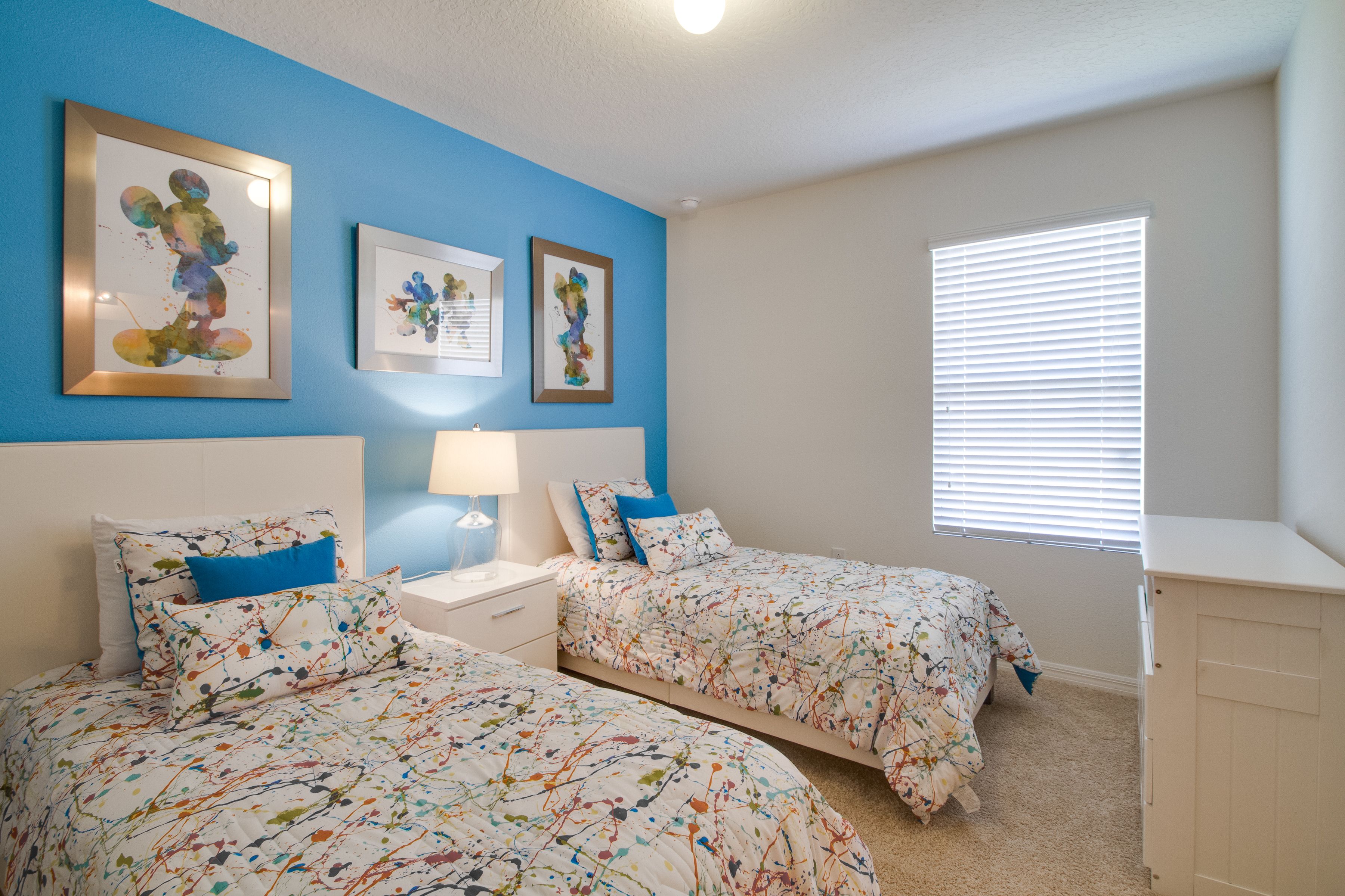 A bedroom with two beds, a nightstand, a lamp, and artwork on the wall.