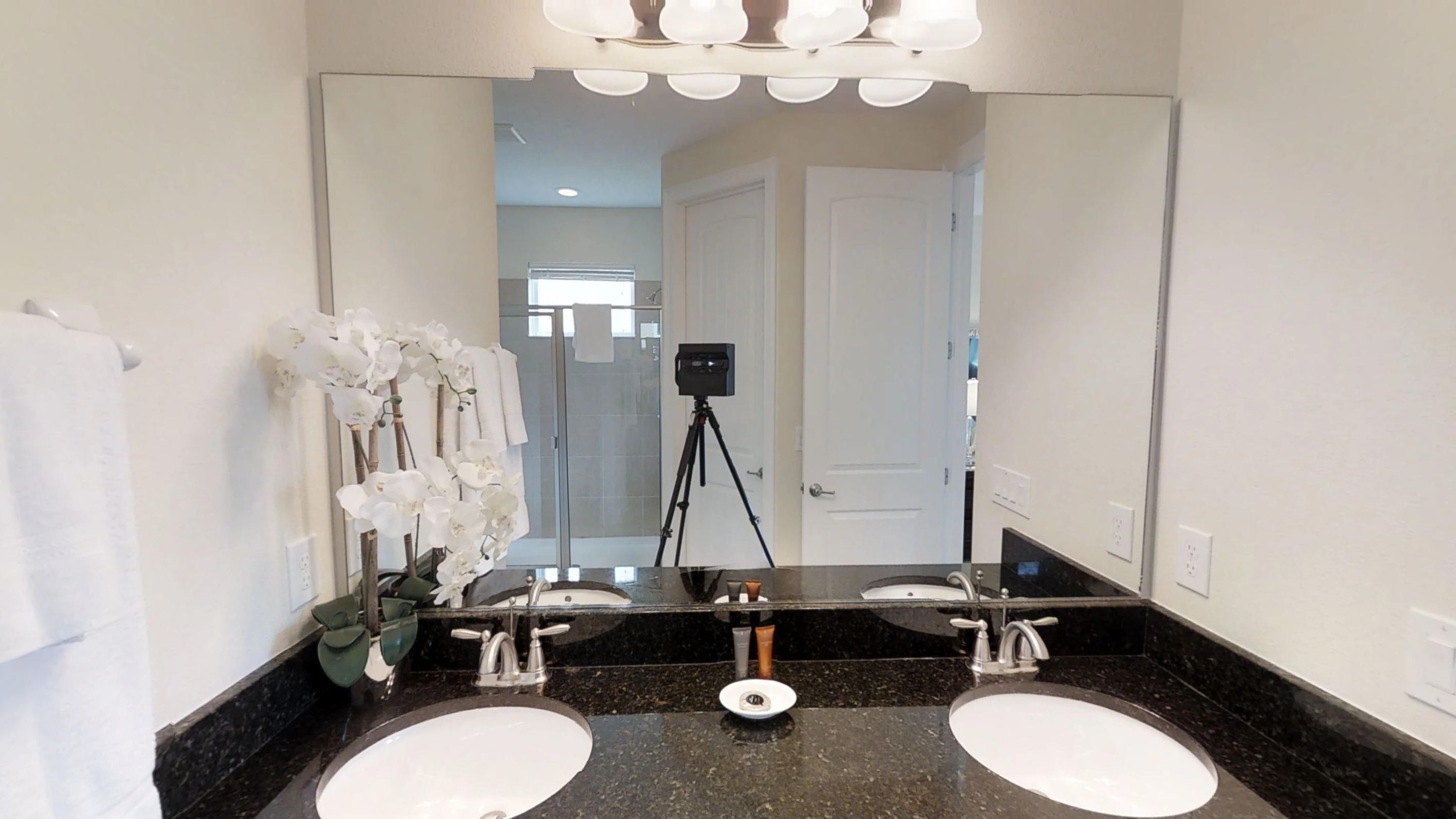 A bathroom with two sinks, a large mirror, and a tripod-mounted camera.