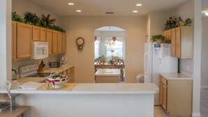 A kitchen with wooden cabinets, a microwave, a refrigerator, and a dining area with a table and chairs. - Highlands Reserve Golf & Country Club 533 (Davenport)