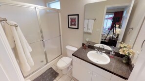 A bathroom with a glass shower enclosure, a toilet, a sink with a mirror, and a small flower arrangement. - Lake Berkley Resort 4715 B (Kissimmee)