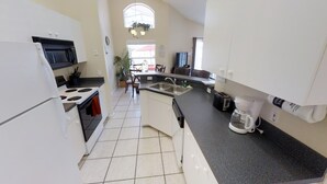 Ett kompakt kök med vita skåp, en spis, ett handfat och en kaffebryggare.