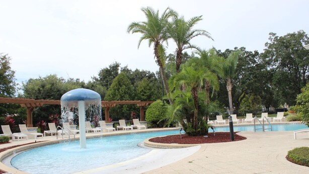 A swimming pool with a water fountain, surrounded by lounge chairs and palm trees.