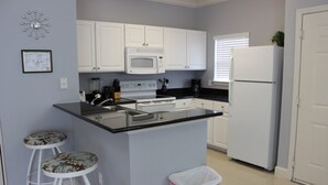 A kitchen with white cabinets, a microwave, a refrigerator, a sink, and two bar stools.