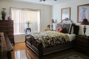 A bedroom with a wooden bed, a dresser, a nightstand, a lamp, and a window with blinds.