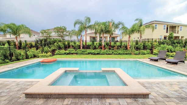 A swimming pool with a hot tub, surrounded by a brick patio, palm trees, and lounge chairs. - Encore Resort at Reunion 281 (Kissimmee)
