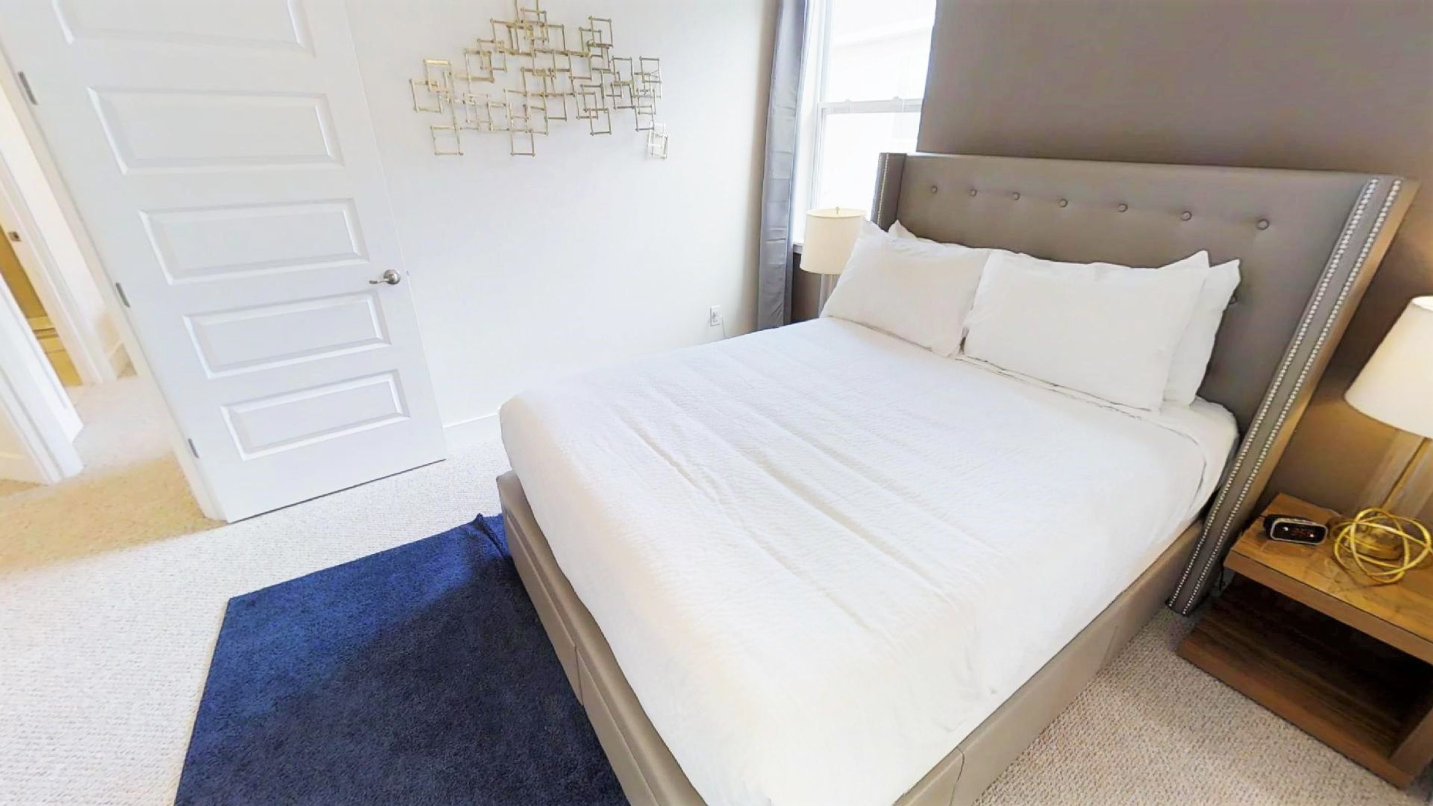 A neatly arranged hotel room with a large bed, a bedside table with a lamp, and a decorative wall piece.