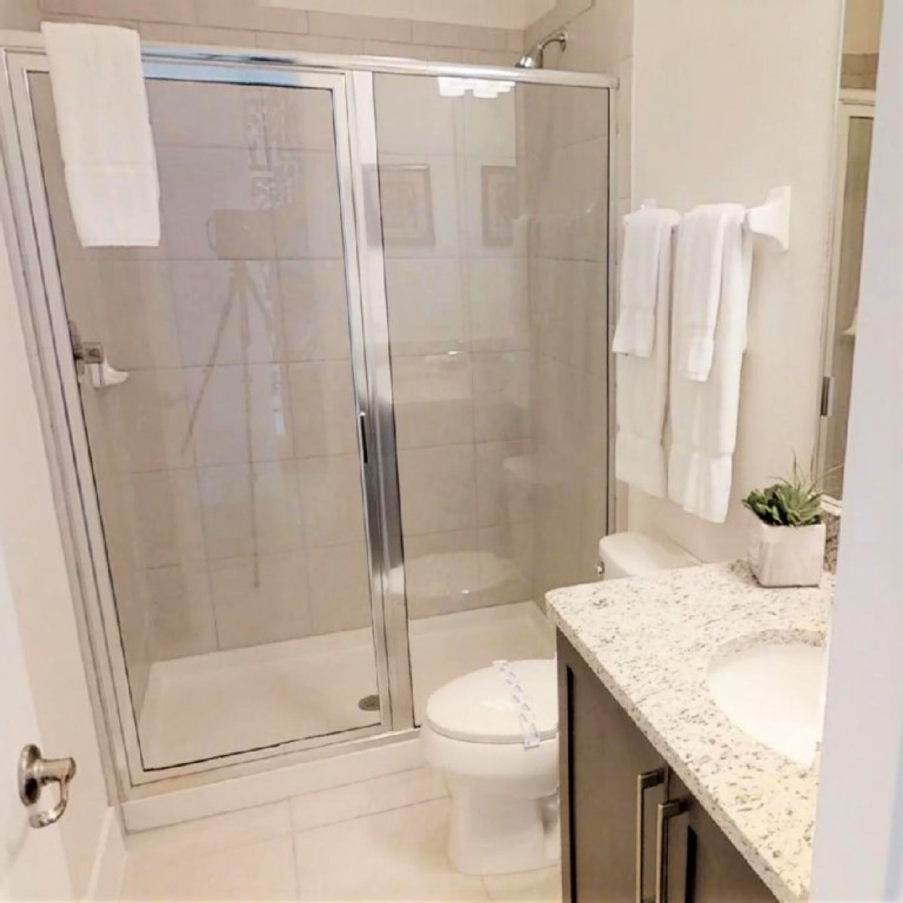 Un baño moderno con ducha envuelta en vidrio, inodoro blanco y encimera de granito.