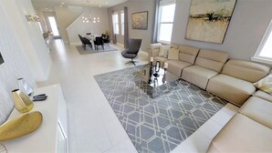 A modern living room with a beige sofa, a patterned rug, and a dining area with a table and chairs. - Encore Resort at Reunion 281 (Kissimmee)