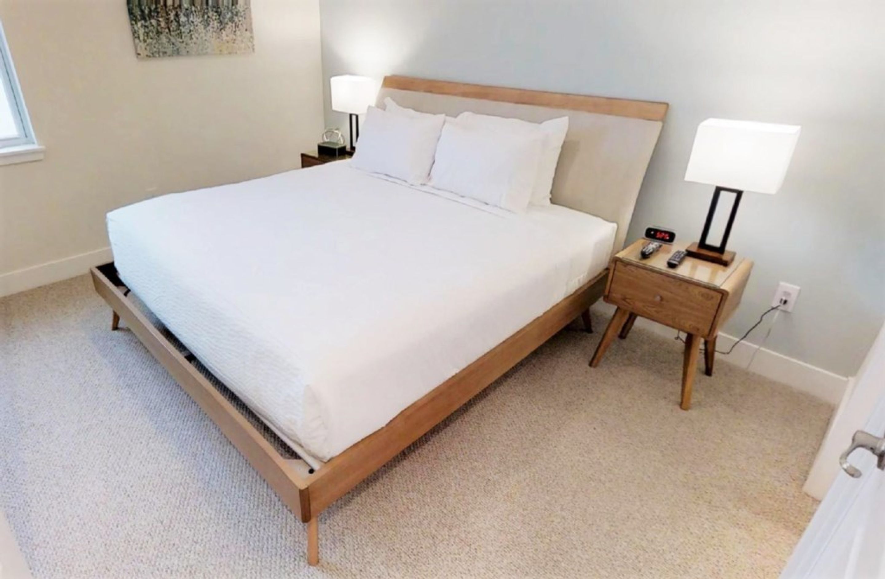 A neatly made bed with a wooden frame, two bedside tables with lamps, and a small bedside clock.
