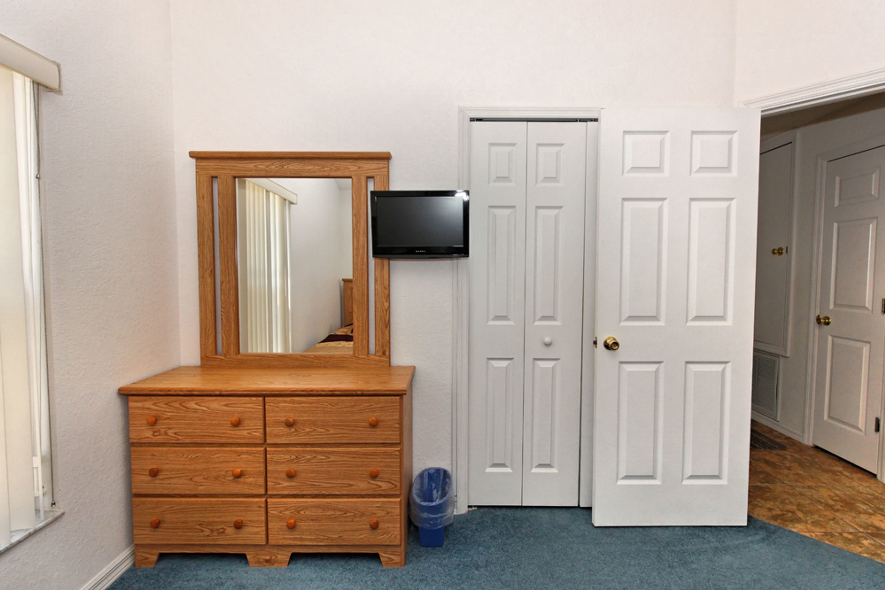 A room with a wooden dresser, a television mounted on the wall, and a white door.