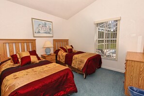 Een slaapkamer met twee bedden, een nachtkastje, een lamp, een raam met tralies en een houten dressoir.