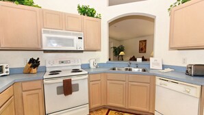 A kitchen with wooden cabinets, a white stove, a microwave, a sink, and a dishwasher. - Highlands Reserve Golf & Country Club 301 (Davenport)