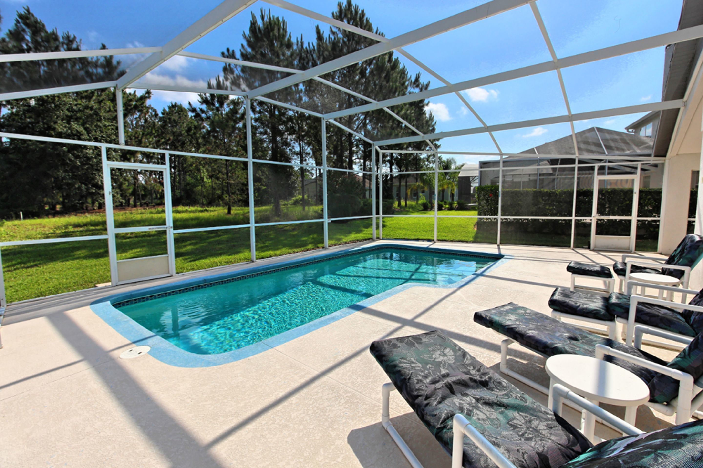 Une piscine avec des chaises longues et un espace patio fermé par des baies vitrées.