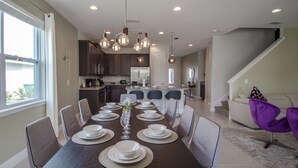 A dining area with a long table set for six, surrounded by chairs, and a kitchen in the background. - Encore Resort at Reunion 480 1825.8 (Kissimmee)