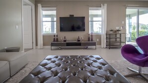 A modern living room with a large tufted sofa, a flat-screen TV mounted on the wall, and a purple chair. - Encore Resort at Reunion 480 1825.8 (Kissimmee)
