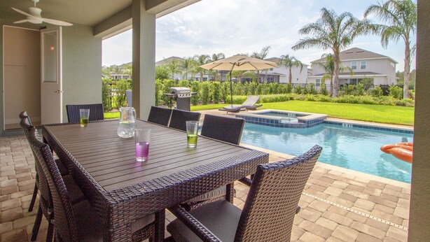 A patio with a table and chairs, a pool, and a view of houses in the background. - Encore Resort at Reunion 480 1825.8 (Kissimmee)