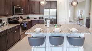 A modern kitchen with dark wood cabinets, stainless steel appliances, granite countertops, and pendant lighting. - Encore Resort at Reunion 480 1825.8 (Kissimmee)