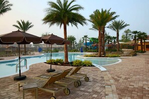 Un espace aménagé au bord de la piscine, avec des chaises longues, des parasols et des palmiers.