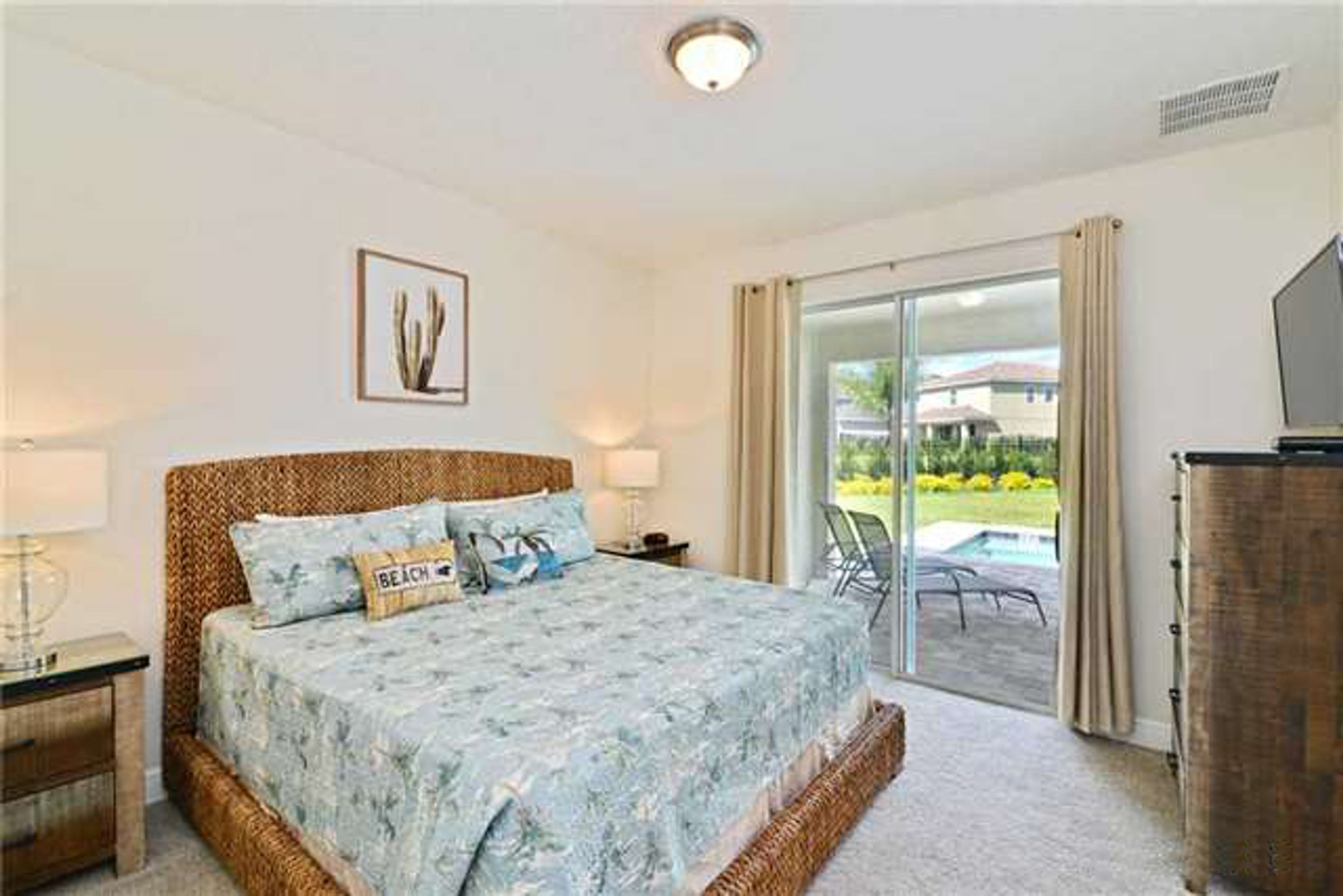 A bedroom with a bed, a nightstand, a lamp, a television, and a sliding glass door leading to a balcony.