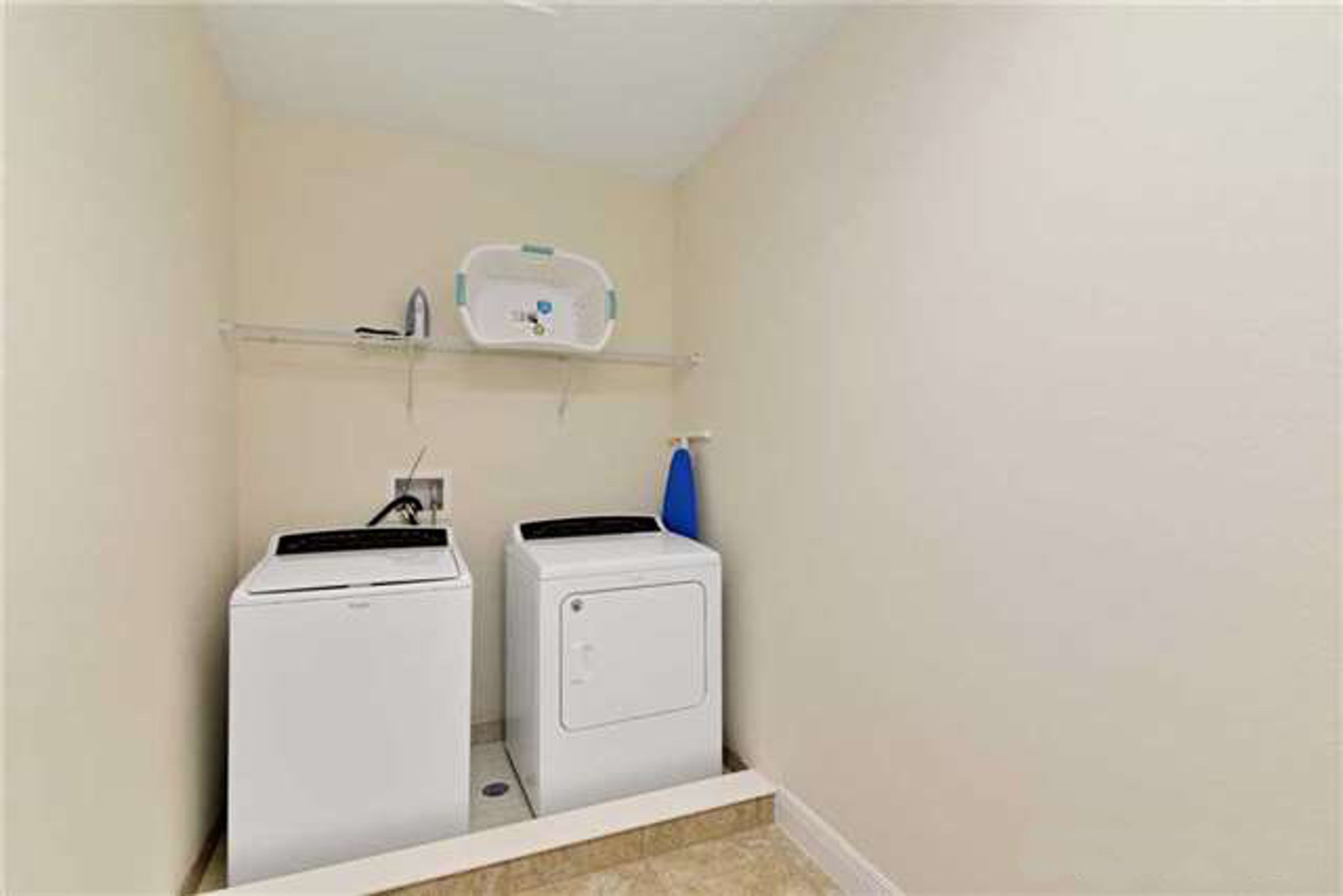 A laundry room with two white washing machines and a shelf above them.