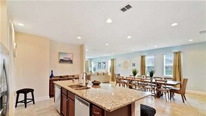 A spacious kitchen with a large island, a dining area with wooden chairs, and a view of the living room. - Encore Resort at Reunion 380 (Kissimmee)