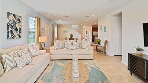 A spacious living room with a beige sofa, patterned cushions, a coffee table, and a staircase leading to another level. - Encore Resort at Reunion 380 (Kissimmee)