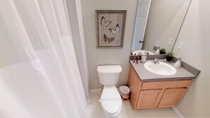 Une salle de bain avec des toilettes, un lavabo et un miroir. Un tableau représentant un papillon, encadré, est accroché au mur.