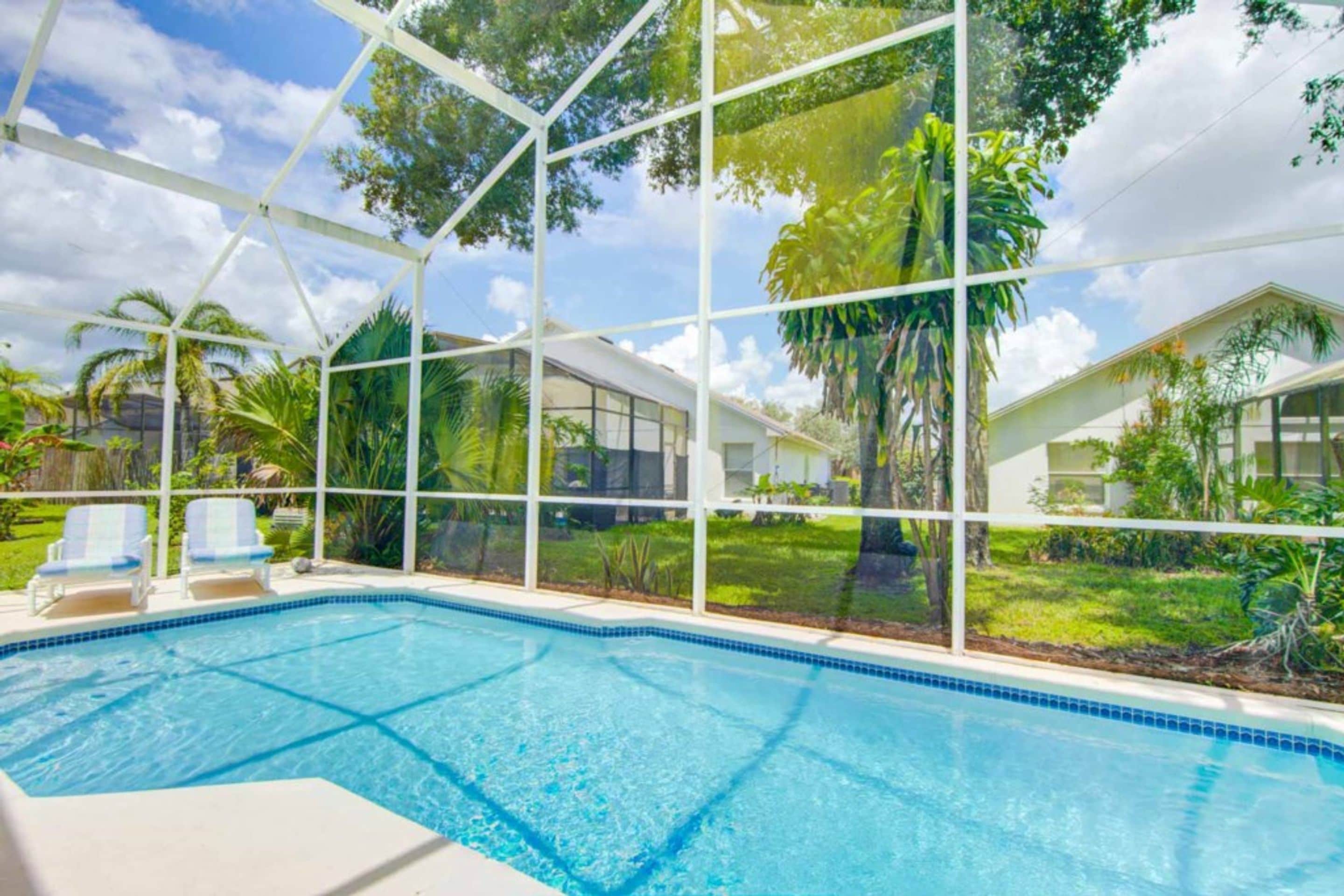 A swimming pool with clear blue water, surrounded by a white fence and glass panels.
