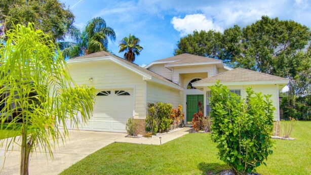 Une maison de plain-pied avec un garage à l’avant, une porte verte et un petit jardin devant, agrémenté d’un palmier et de quelques arbustes.