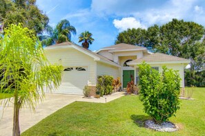 A single-story house with a front garage, a green door, and a small front yard with a palm tree and shrubs. - Creekside 4321 (Kissimmee)